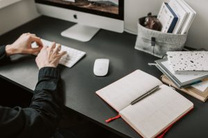 person typing on mac with notebook on the table